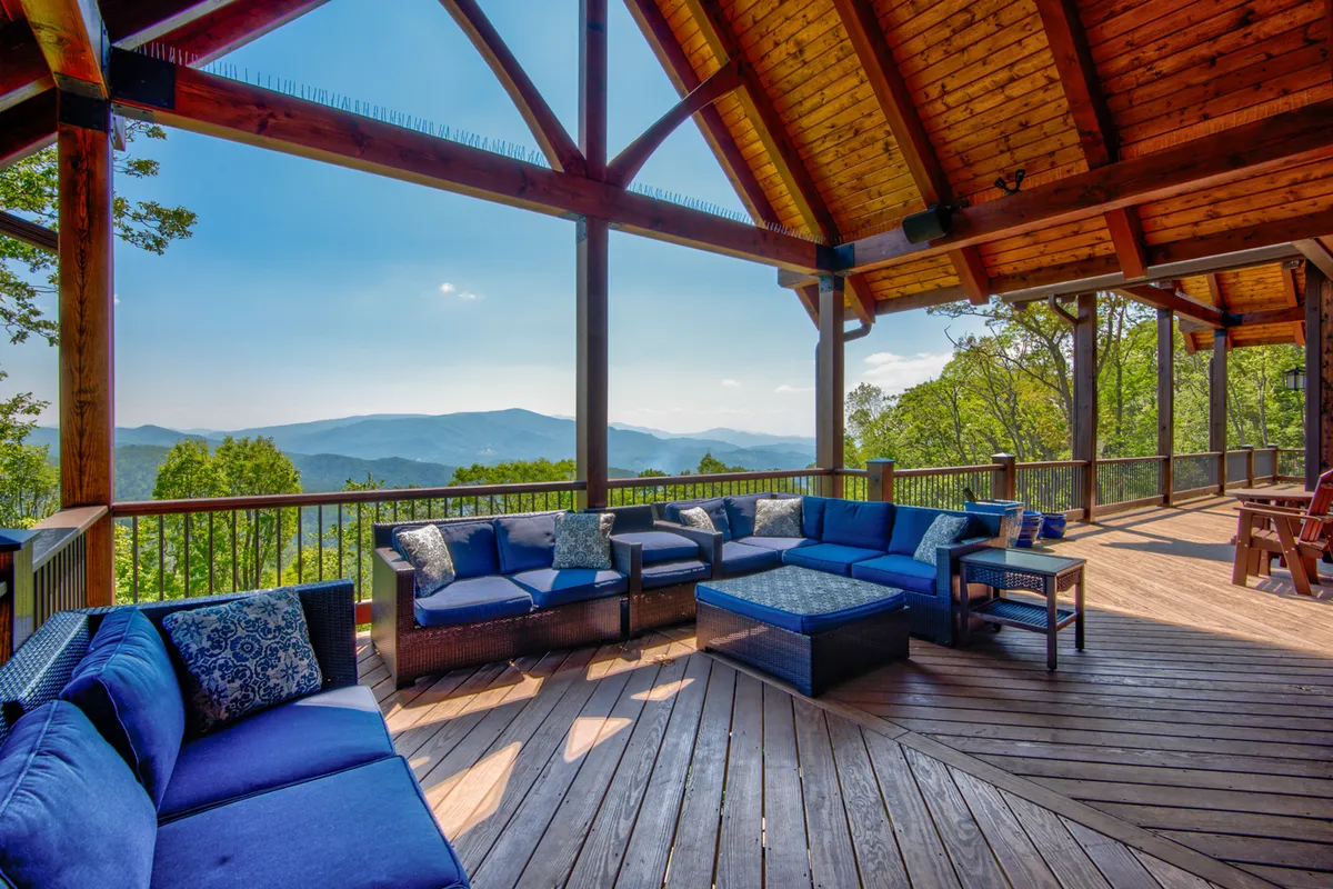 An expansive outdoor deck with ample seating and dramatic mountain views, framed by sturdy wooden beams. The scene is set for sunset toasts, al fresco grilling, and lively outdoor gatherings under the sky.