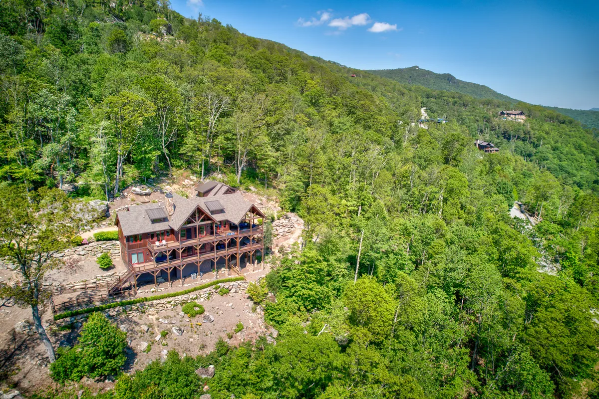 A tranquil exterior shot highlighting the house nestled among trees and rocky landscape, with inviting outdoor gathering spaces for morning coffee or evening stargazing. The scene radiates serenity and a direct connection to the natural surroundings.