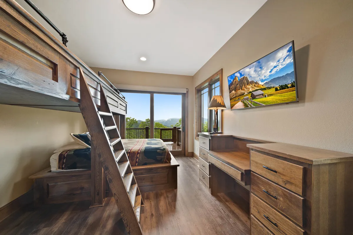 A custom-designed bunk room with built-in beds, large windows that frame stunning mountain views, a wooden desk, and television. The playful, cozy environment is perfect for children or adventurous guests, blending style with functionality.