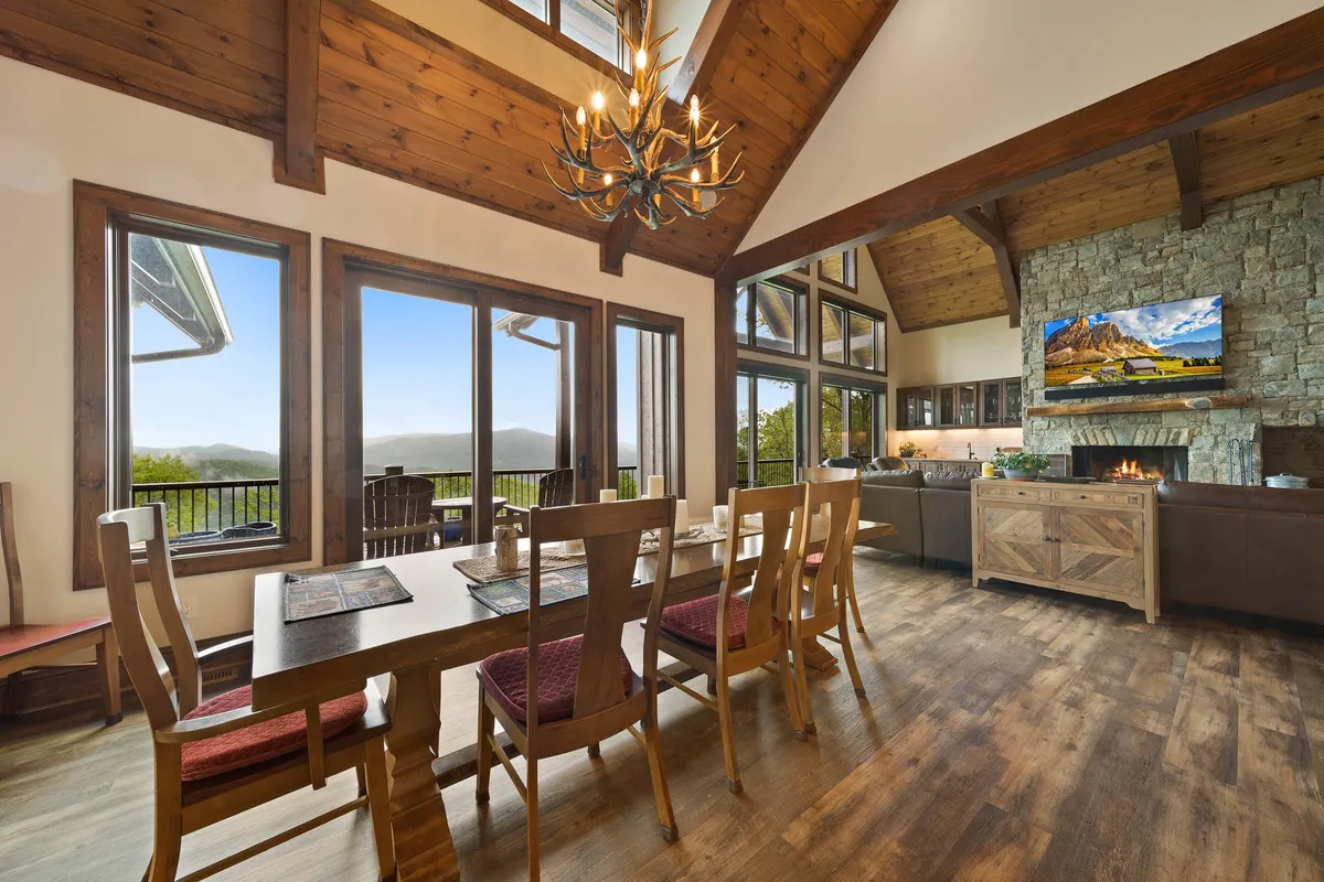 A cozy dining area featuring a large wooden table, chandelier, fireplace, and windows framing mountain vistas. This space feels intimate yet grand, ideal for festive feasts or relaxed family meals while taking in the sunset.