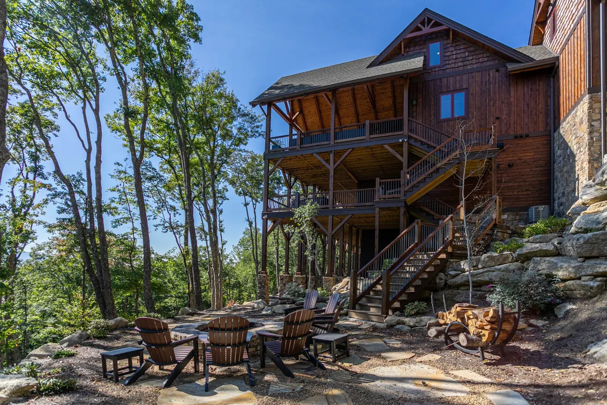 A cozy outdoor fire pit area with wooden chairs on a spacious deck overlooking natural rock formations and the forest beyond. The space is designed for evening gatherings, s’mores, and storytelling as the sun sets over the mountains.
