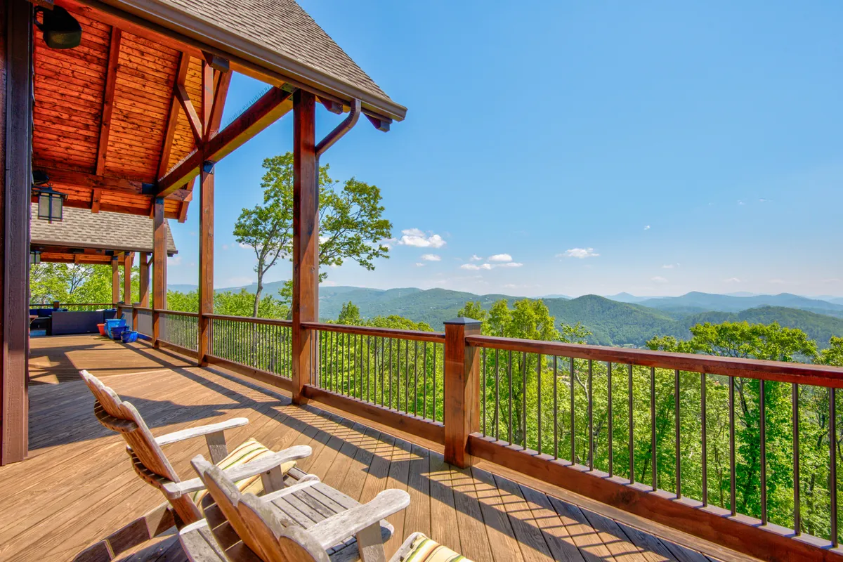 This image features a spacious wooden deck furnished with comfortable chairs, overlooking breathtaking mountain views and surrounded by lush green trees under a clear blue sky. The setting is ideal for relaxing, socializing, or holding group activities while immersed in nature.