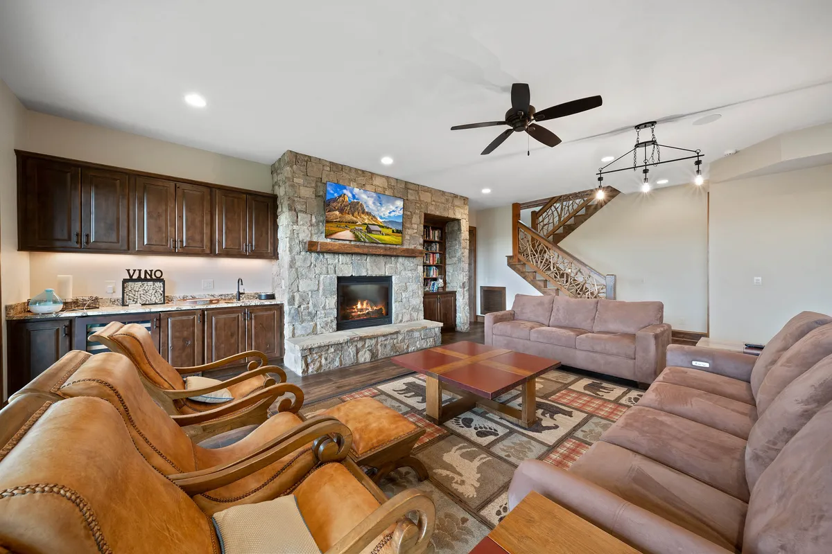 A cozy entertainment lounge featuring a prominent stone fireplace, a large flat-screen TV mounted above wooden cabinetry, and a plush sectional seating area. The space feels warm and inviting, ideal for family gatherings, movie nights, or relaxing with friends after outdoor adventures.