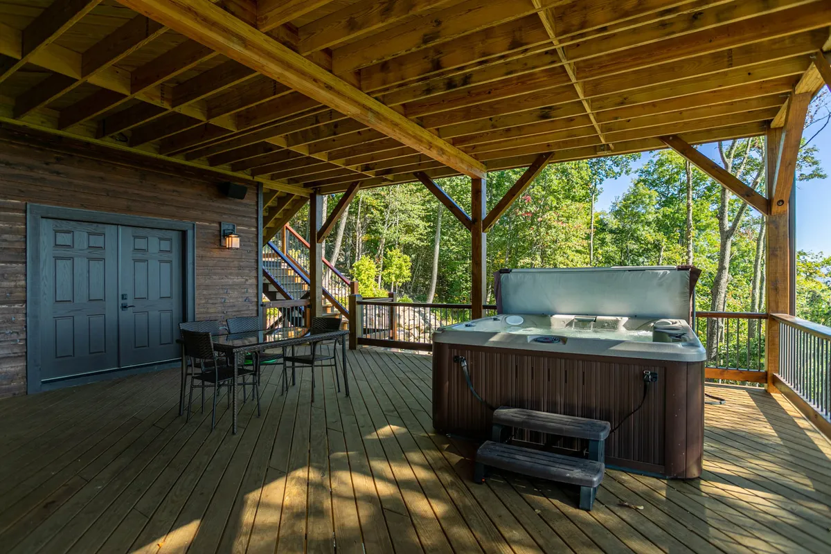 An inviting exterior deck scene with a bubbling hot tub, comfortable seating, and sturdy wooden beams. The area overlooks beautiful sunset skies and mountain views, offering a relaxing retreat after a day full of outdoor activities.